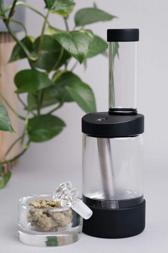 A glass bong with a green leaf design is on a wooden table. Smoke is visible inside, indicating recent use.